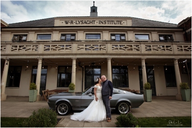 bride and groom kiss by a Ford Mustang