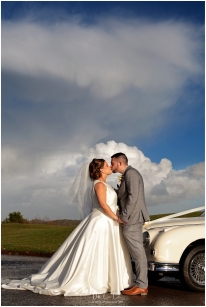 bride and groom kissing against dramatic clouds and blue sky